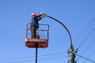 electrician climb work installing new street lamp on electricity power concrete pole in blue sky